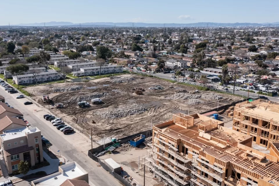 Aerial view of large construction site and vacant, graded lot next to public housing buildings in Watts, Los Angeles, California.